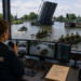 Operator in a Brugoperator Bedienencentrale control room watching a river parade of green military boats through multiple screens and radios in use.